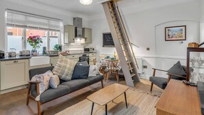A modern kitchen with a built-in oven, a dining area with a table and chairs, a sofa, and a staircase leading to an upper level.