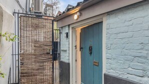 A blue door with a small mailbox and a number plate, a black gate with a woven pattern, and a white brick wall.
