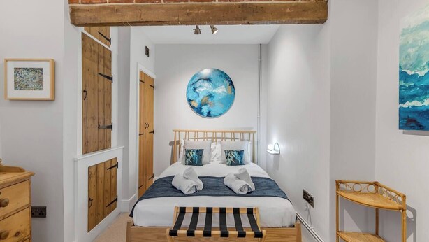 A bedroom with a wooden bed, a round wall art, a wooden bench, and a small shelf.