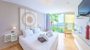 A hotel room with a large bed, a nightstand, a TV, and a balcony with a view of palm trees. - Los Nisperos de Paco (Canillas de Albaida)