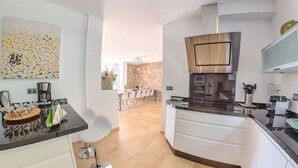 A modern kitchen with white cabinets, a black countertop, and stainless steel appliances. There is a dining area visible in the background with a table and chairs. - Los Nisperos de Paco (Canillas de Albaida)