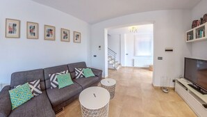 A modern living room with a grey sofa, patterned cushions, a TV, and a staircase leading to another room. - Los Nisperos de Paco (Canillas de Albaida)