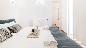Hotelkamer met een bed, kussens, een dienblad met bekers en een vaas, en uitzicht op de gang.