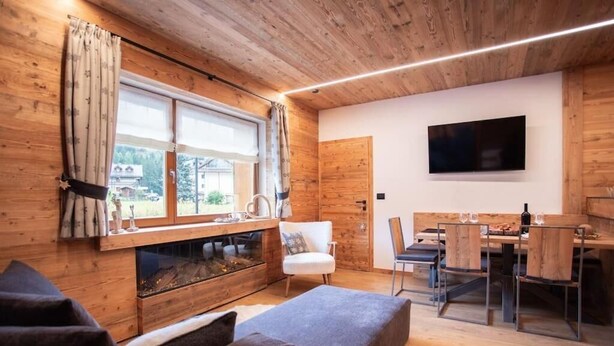 Ein gemütliches Cabin-Interieur mit Holzbalkendecke, Kamin, Essbereich mit Tisch und Stühlen sowie einem an der Wand befestigten Fernseher.