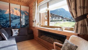 Ein gemütliches Zimmer mit Holzvertäfelung, einem Kamin, einer Couch und einem Fenster mit Blick auf die Berge.