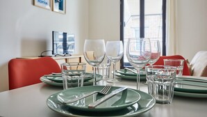 A dining table set with green plates, clear glasses, and cutlery, with a red chair and a window in the background.