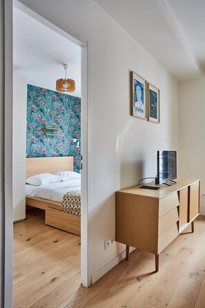 Un dormitorio con cama de madera, un escritorio con computadora y una pared de papel tapiz floral.