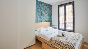 A bedroom with a bed, a window with a view, and a wall with floral wallpaper.