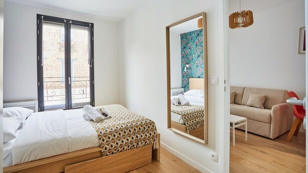 A bedroom with a bed, a mirror, a window, and a sofa.