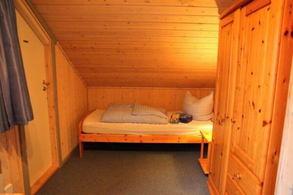 Una habitación pequeña con cama individual, paredes de madera y techo inclinado.