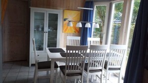 Un comedor con una mesa y sillas blancas, un aparador de vidrio y un cuadro en la pared.