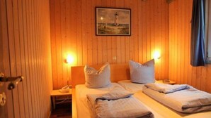 Una habitación acogedora con paredes de madera, una cama con almohadas, una mesita de noche y un cuadro de un faro.