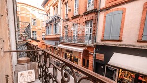 Una calle estrecha con edificios que tienen balcones y tiendas, incluyendo una cafetería.