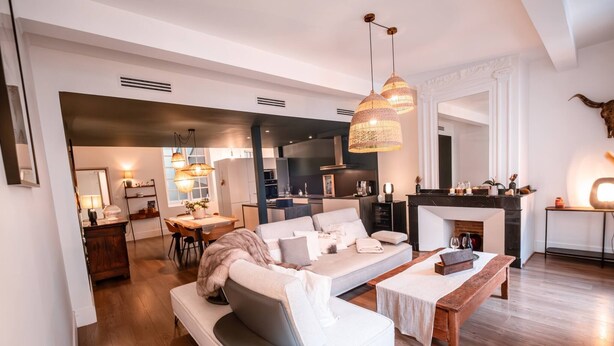 Una sala de estar moderna con un sofá, una mesa de centro y una zona de comedor. Se ve una chimenea y una cocina al fondo.