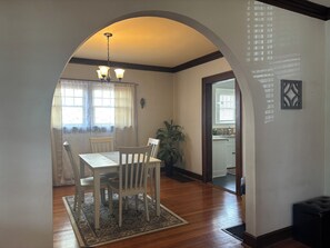 A dining area with a table and chairs, a chandelier, a patterned rug, and a view into the kitchen.