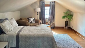 Une chambre à coucher avec un lit, un canapé, une lampe, une plante et une vue sur l’extérieur par une fenêtre.