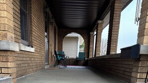 Un escalier extérieur abrité, menant à l’entrée d’un bâtiment, avec des murs en briques et une rampe en métal.