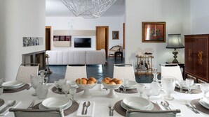 A dining area with a table set for a meal, a sofa in the background, and a television on the wall. - Villa in Trapani With Private Pool & Near Sea (Paceco)