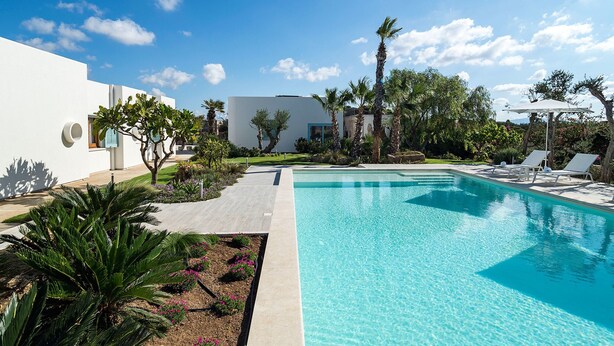 A modern pool area with a clear blue pool, surrounded by palm trees and a white building. - Villa in Trapani With Private Pool & Near Sea (Paceco)