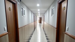A long, narrow hallway with wooden doors on both sides, white tiled floors, and recessed ceiling lights. - Hotel Sunbright Residency - Manipal (Udupi)