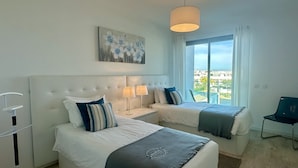 A hotel room with two beds, a large window with a view, a painting on the wall, and a chair.