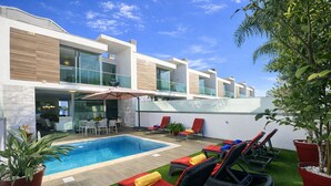 A modern outdoor pool area with a rectangular pool, lounge chairs, and a dining area with outdoor seating.