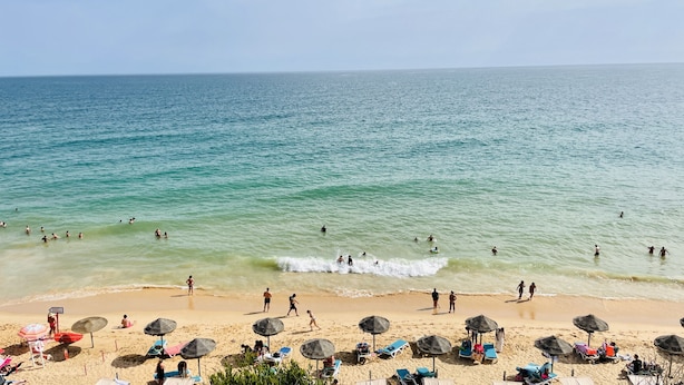 A beach with clear turquoise water, people swimming and walking along the shore, and beach umbrellas and lounge chairs.