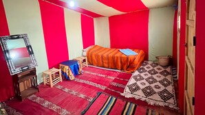Une chambre à coucher avec un lit, une petite table, un miroir et un mur à rayures rouges et blanches.