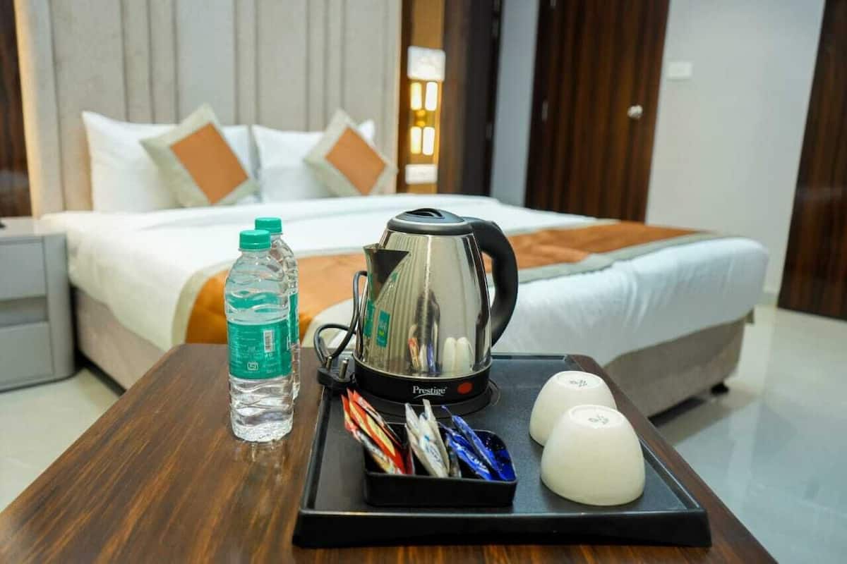 A neatly made bed with pillows, a bedside table with a kettle, water bottle, and tea bags.
