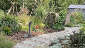 Un vialetto in pietra che si snoda attraverso un giardino con diverse piante e un muro di pietra.