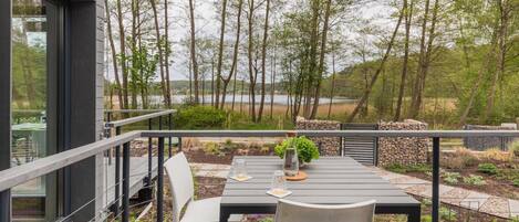 A deck with a table and chairs overlooking a lake, surrounded by trees.