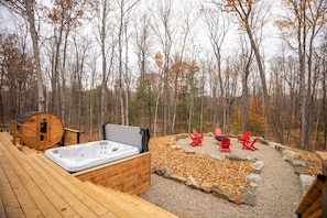 Una terraza de madera con un jacuzzi y sillas Adirondack rojas en un área boscosa.