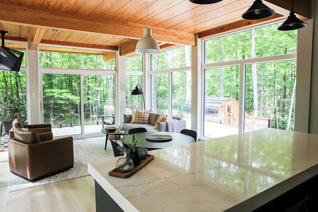 A modern kitchen with large windows, a dining area, and a cozy seating space with a view of the forest.