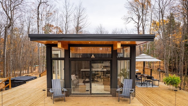 Una cabaña moderna con entrada de vidrio, terraza de madera y zona de estar al aire libre.