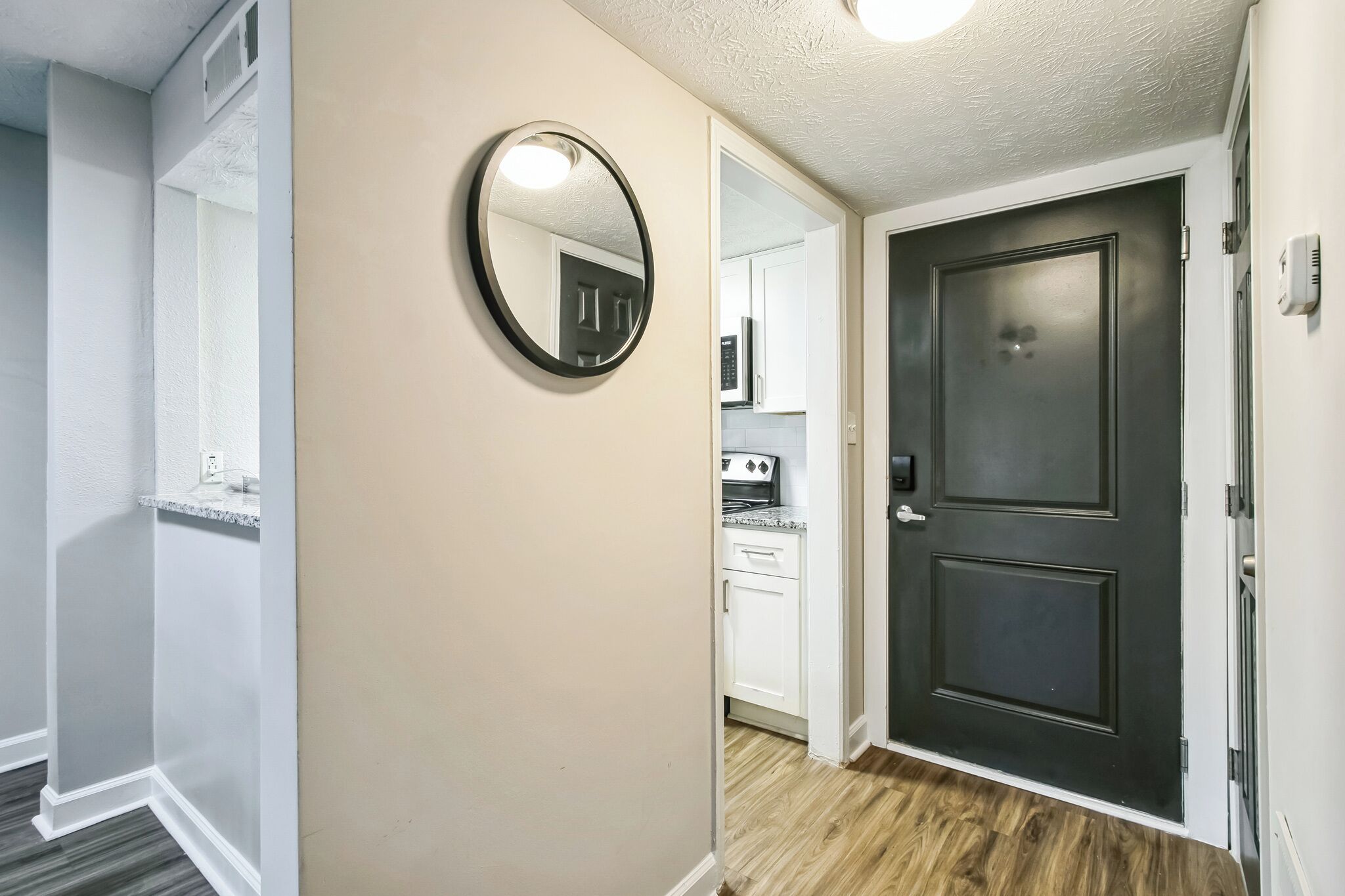 A hallway with a dark door, a white wall, and a round mirror.