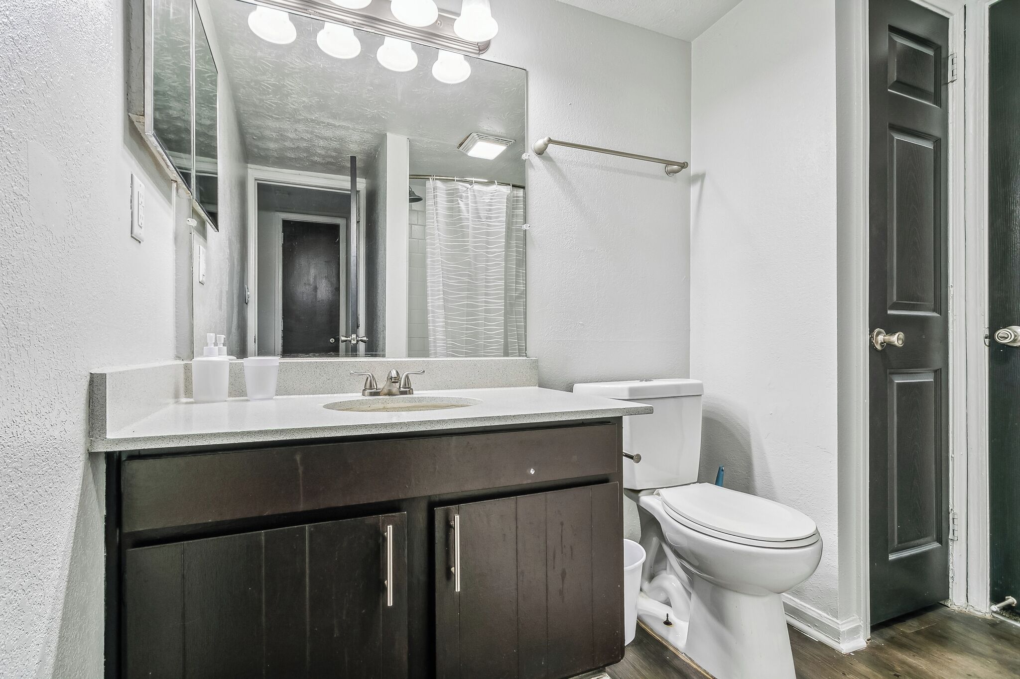 A bathroom with a white sink, dark cabinets, a white toilet, and a mirror with lights.