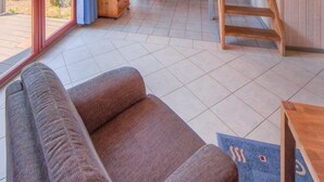 Un'ampia zona giorno con soffitto alto, una scala in legno e un'area pranzo con vista sull'esterno.