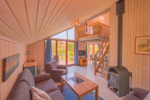 A cozy cabin interior with a living area, sofa, coffee table, fireplace, and a staircase leading to an upper deck. - Skandinavisches Ferienhaus in Mirow (Mirow)