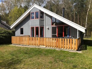 A two-story building with a wooden deck, large windows, and a chimney. - Skandinavisches Ferienhaus in Mirow (Mirow)