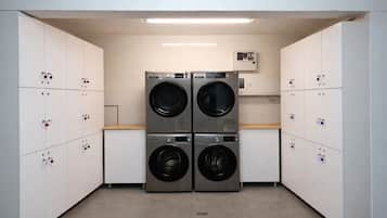A laundry room with four stacked front-loading washing machines, a control panel above, and a row of lockers on either side.