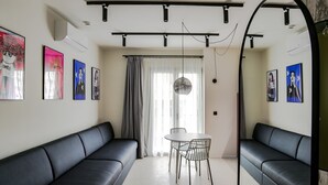 A modern living room with black leather sofas, a round dining table with chairs, and artwork on the walls.