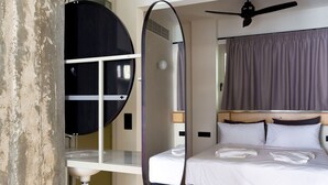 A compact hotel room with a bunk bed, a small desk with a mirror, a ceiling fan, and a shower area.