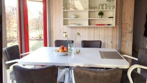 A dining area with a white table, grey chairs, and a wooden wall with shelves. - Skandinavisches Ferienhaus in Mirow (Mirow)