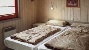 A room with wooden walls and a window. There are two beds with white linens and a single bedside table with a lamp. - Skandinavisches Ferienhaus in Mirow (Mirow)
