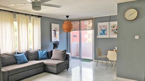Een moderne woonkamer met een grijze hoekbank, een plafondventilator en een eethoek met een tafel en stoelen.