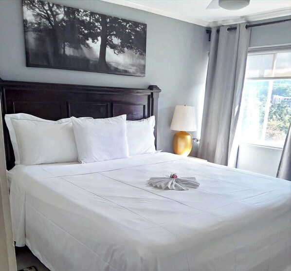 A neatly made bed with white linens, a dark wooden headboard, and a wall-mounted painting of trees.