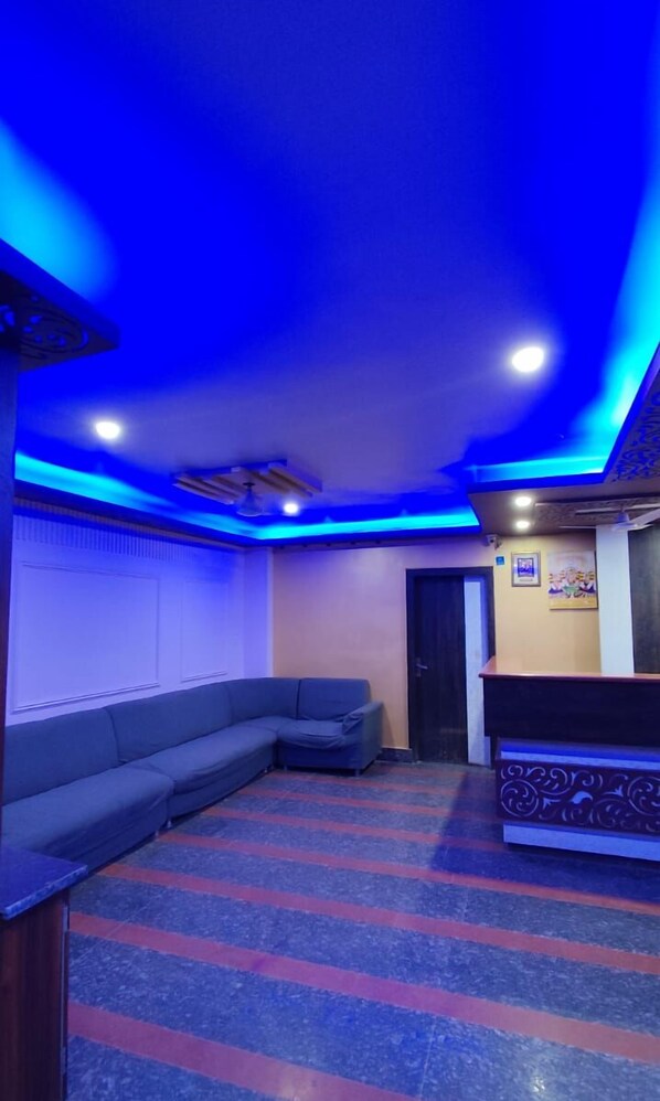 Une pièce avec un plafond éclairé en bleu, un canapé, un comptoir d’accueil et un tapis à motifs.