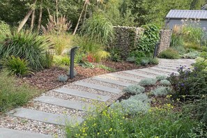 A garden pathway with a stone border, surrounded by various plants and a stone wall. - Holiday Home by Lake Wiselka, Near Baltic Beach (gmina Wolin)