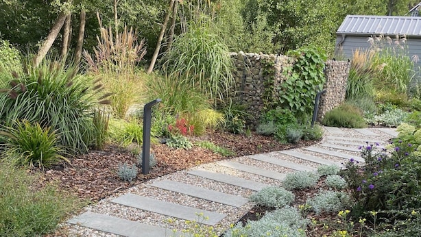 Ein Gartenweg mit trittfesten Steinen, umgeben von verschiedenen Pflanzen und einer Steinmauer.