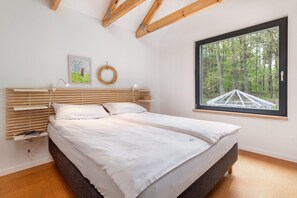 A bedroom with a large bed, a window with a view of trees, a wall-mounted light, and a framed picture.